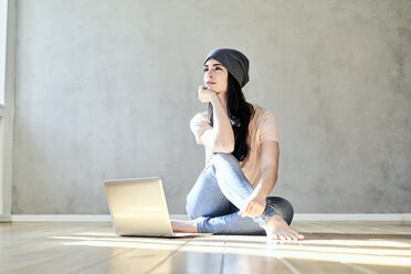 Nachdenkliche junge Frau sitzt mit Laptop auf dem Boden - FMKF03984