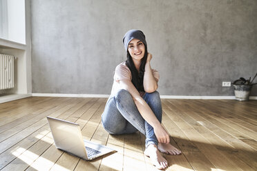 Lächelnde junge Frau auf dem Boden sitzend mit Laptop - FMKF03986