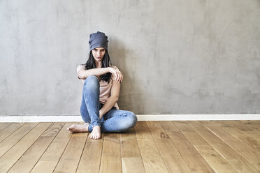 Young woman sitting on the floor in sparse room - FMKF03990