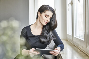 Lächelnde junge Frau mit Tablet am Fenster - FMKF04000