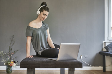 Young woman with headphones sitting on lounge using laptop - FMKF04015