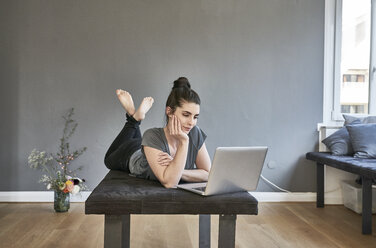 Junge Frau auf dem Sofa liegend mit Laptop - FMKF04017