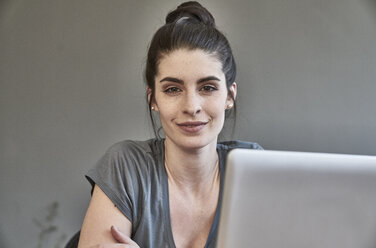 Portrait of smiling young woman with laptop - FMKF04018
