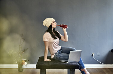 Young woman with laptop drinking from bottle - FMKF04022