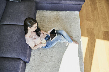 Young woman using tablet at home in living room - FMKF04032