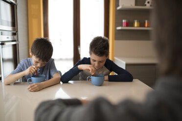 Zwei Jungen essen Seite an Seite am Küchentisch - ZOCF00211