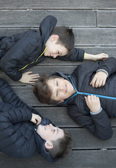 Drei Freunde in schwarzen Kapuzenjacken liegen zusammen auf einer Terrasse - ZOCF00217