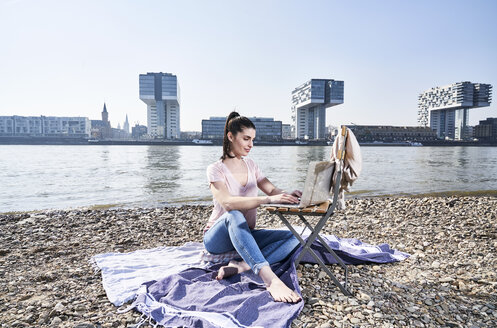 Deutschland, Köln, junge Frau mit Laptop am Rhein - FMKF04046