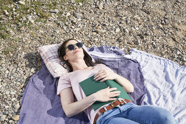 Young woman lying on blanket with book - FMKF04048