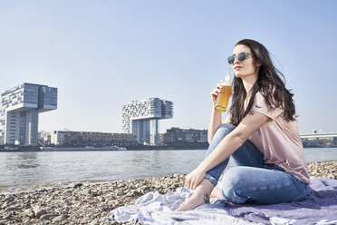 Deutschland, Köln, junge Frau entspannt sich und trinkt ein Bier am Rhein - FMKF04053