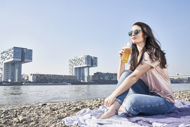 Germany, Cologne, young woman relaxing and having a beer at River Rhine - FMKF04053