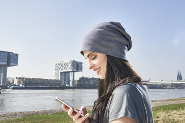 Germany, Cologne, smiling young woman using cell phone at River Rhine - FMKF04062