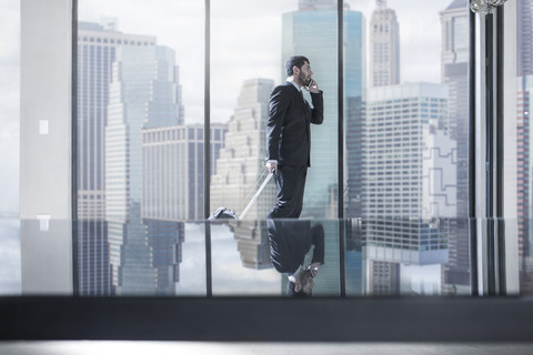 Geschäftsmann mit Rollkoffer am Telefon in einem städtischen Büro, lizenzfreies Stockfoto