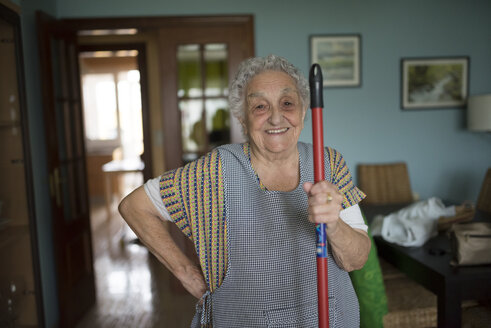 Porträt einer lächelnden älteren Frau, die einen Wischmopp in der Hand hält - RAEF01864