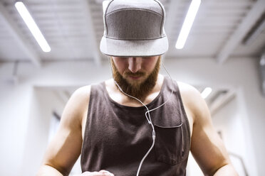 Junger Sportler mit Mütze und Kopfhörern im Fitnessstudio - HAPF01538