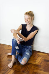 Ginger woman sitting on floor at home, drinking red wine - VABF01337