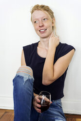 Ginger woman sitting on floor at home, drinking red wine - VABF01338