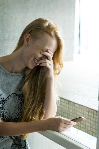 Junge Frau hält Smartphone, lachend, lizenzfreies Stockfoto