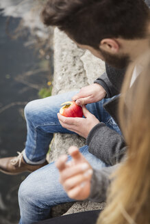 Couple sitting on wall peeling apple - MIDF00823