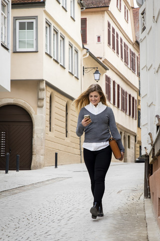 Germany, Tuebingen, smiling young student looking at cell phone while walking stock photo