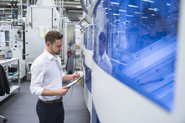 Mann macht sich Notizen an einer Maschine in einer Fabrikhalle - DIGF02157