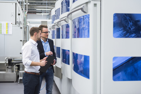 Zwei Männer unterhalten sich in einer Fabrikhalle und betrachten eine Maschine, lizenzfreies Stockfoto