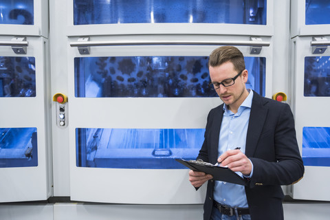 Man taking notes at machine in factory shop floor stock photo