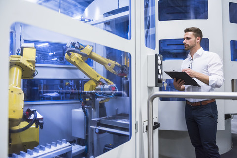 Man taking notes at robotics machine in factory shop floor stock photo