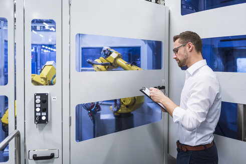 Mann macht sich Notizen an einer Robotikmaschine in einer Fabrikhalle - DIGF02167