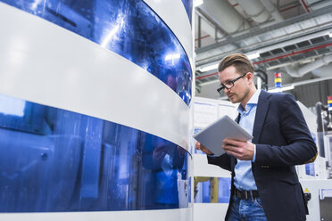 Man holding tablet looking at machine in factory shop floor - DIGF02171