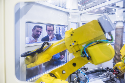 Zwei Männer in einer Fabrikhalle mit Blick auf eine Robotikmaschine, lizenzfreies Stockfoto