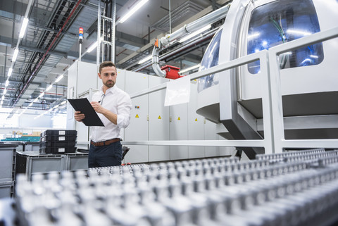 Mann macht sich Notizen in einer Fabrikhalle, lizenzfreies Stockfoto