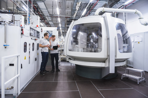 Two men talking at machine in factory shop floor stock photo