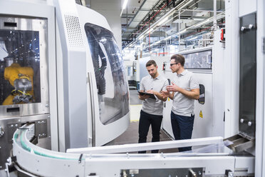 Two men talking at machine in factory shop floor - DIGF02194