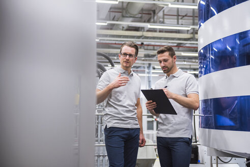 Zwei Männer sprechen an einer Maschine in einer Fabrikhalle - DIGF02196