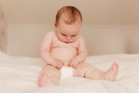 Baby-Mädchen sitzt auf dem Bett und untersucht die Windeln, lizenzfreies Stockfoto