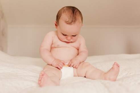 Baby-Mädchen sitzt auf dem Bett und untersucht die Windeln - NMSF00061