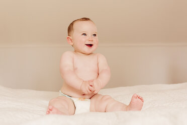 Porträt eines glücklichen kleinen Mädchens auf dem Bett sitzend - NMSF00062