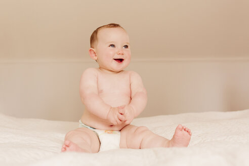Portrait of happy baby girl sitting on bed - NMSF00062