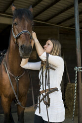 Young woman applying bridle to horse - ZOCF00234