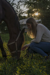 Junge Frau mit Pferd auf einer Wiese bei Sonnenuntergang - ZOCF00249