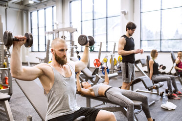 Junger Mann beim Training mit Hanteln im Fitnessstudio - HAPF01575