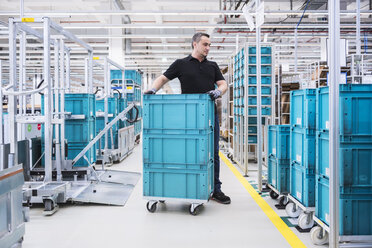 Man at tugger train organising boxes in industrial hall - DIGF02209