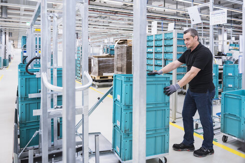 Mann am Schlepperzug ordnet Kisten in der Industriehalle - DIGF02210