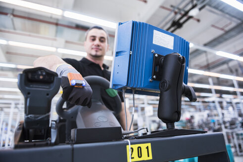 Mann mit tragbarem Scanner auf einem Schlepper in einer Fabrikhalle - DIGF02211