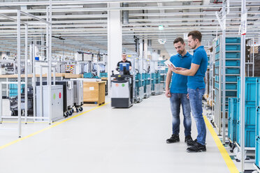 Two men with tablet talking in industrial hall while man driving a tugger train - DIGF02216