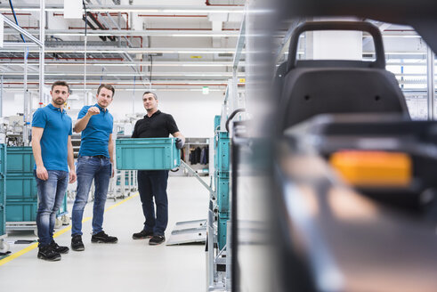 Zwei Männer instruieren einen Arbeiter mit einer Kiste in einer Industriehalle - DIGF02220