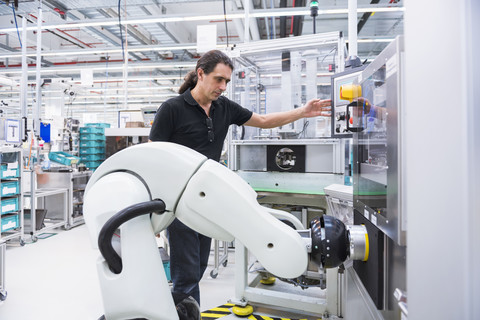 Mann mit Montageroboter in Fabrik, lizenzfreies Stockfoto