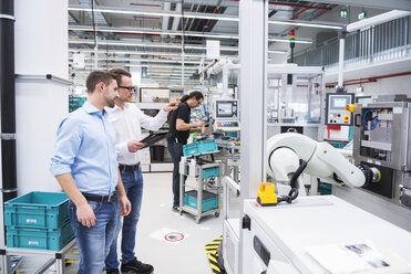 Zwei Männer unterhalten sich in einer Fabrikhalle, während im Hintergrund ein Mann arbeitet - DIGF02238