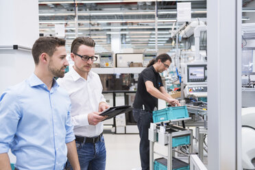 Two men talking in factory shop floor with man in background working - DIGF02239